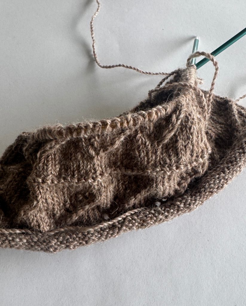 Close-up of brown alpaca cowl in progress, textured knit pattern on needles.