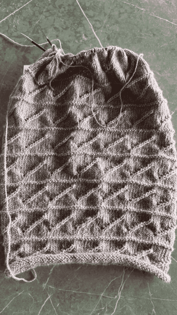 Hand-knit cowl in a geometric accordion pattern, grape-coloured yarn, laid flat.